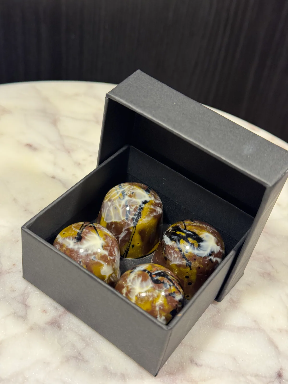 Vier gemarmerde chocoladecreaties in een open zwarte geschenkdoos.